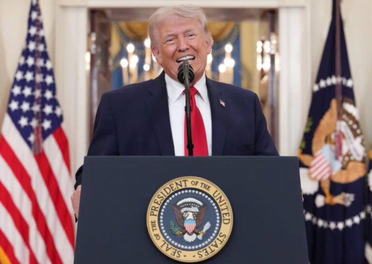 Donald Trump hablando en un podio con la bandera de Estados Unidos de fondo.
